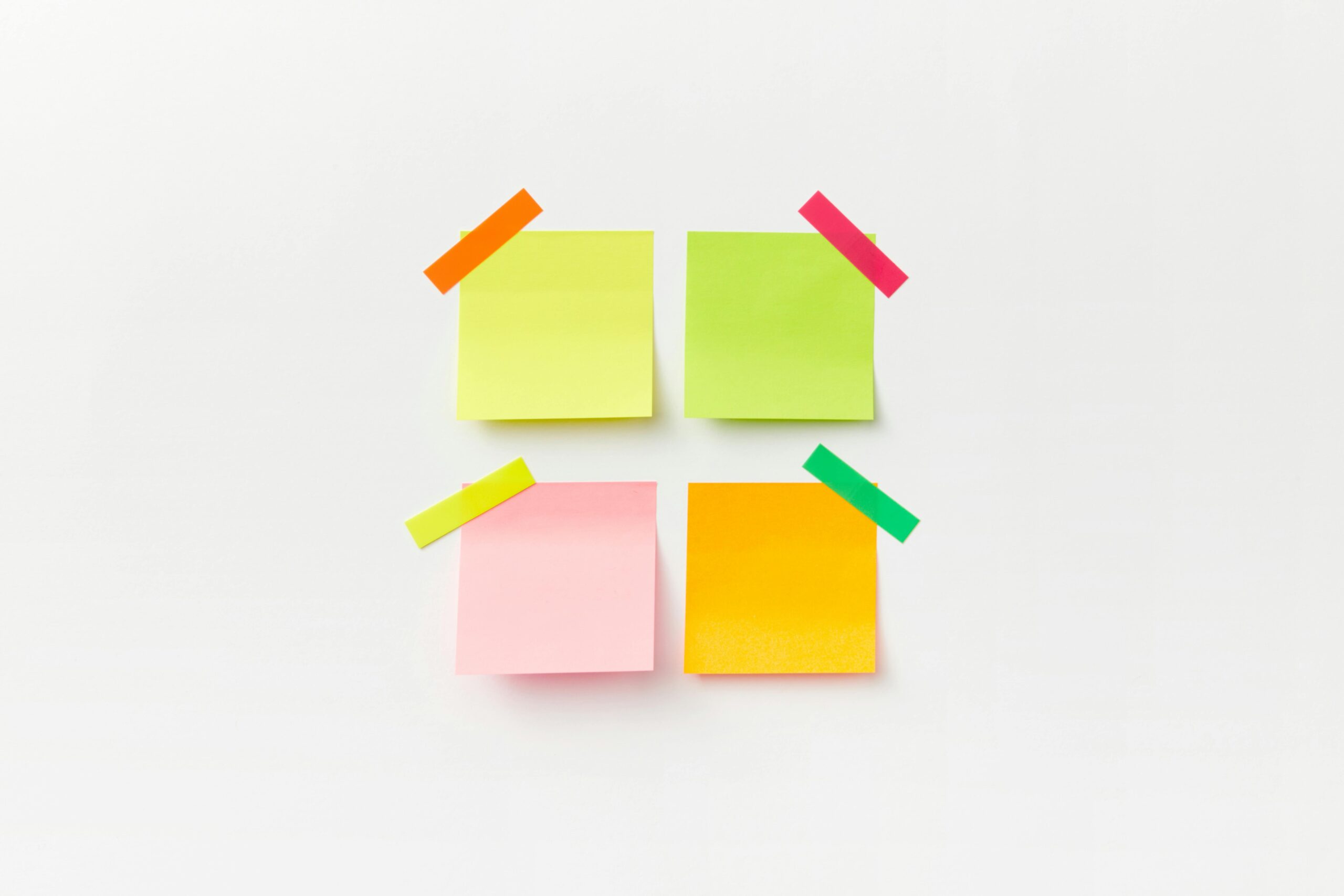 Four colorful sticky notes on white backdrop with vibrant tape. Perfect for office or organizational themes.